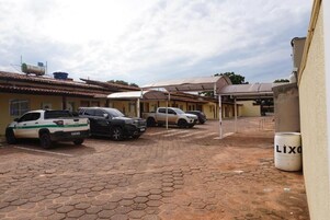 Un estacionamiento con varios vehículos, una pasarela cubierta y un edificio con techo de tejas.