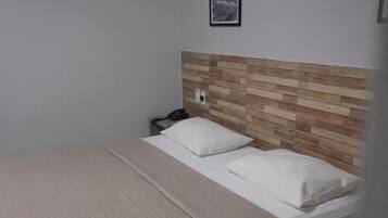 Uma cama de solteiro com cabeceira de madeira, mesa de cabeceira com telefone e um quadro na parede.