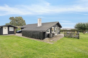A small, single-story building with a sloped roof and a chimney, surrounded by a grassy yard and a wooden fence. - Holiday home in Horne with sea view (Faaborg)