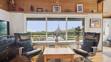 A modern living room with two leather chairs, a wooden coffee table, and a large window offering a view of the outdoors.