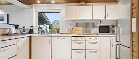 Une cuisine moderne avec des armoires blanches, un réfrigérateur en acier inoxydable, un four à micro-ondes et un plafond en bois.