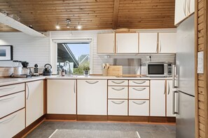 A modern kitchen with white cabinets, a stainless steel refrigerator, a microwave, and a wooden ceiling. - Holiday home in Horne with sea view (Faaborg)
