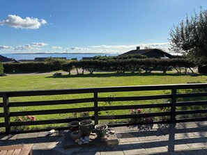 A grassy outdoor area with a wooden fence, potted plants, and a view of the sea.