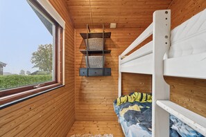 Una camera in una baita di legno con letti a castello, una finestra e uno scaffale con cesti.