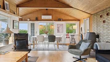 Een ruime kamer met een hoog houten plafond, een eethoek met een tafel en stoelen, en een zithoek met banken en een salontafel.