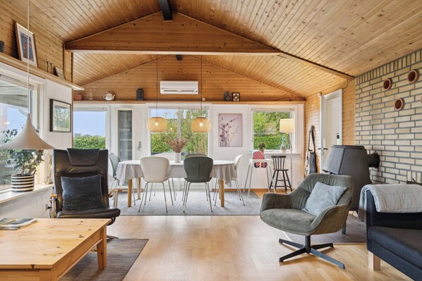 Una habitación amplia con un techo de madera alto, una zona de comedor con mesa y sillas, y un área de descanso con sofás y una mesita de centro.