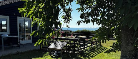 En græsbelagt udendørs arealer med en træterrasse og en bygning i baggrunden.