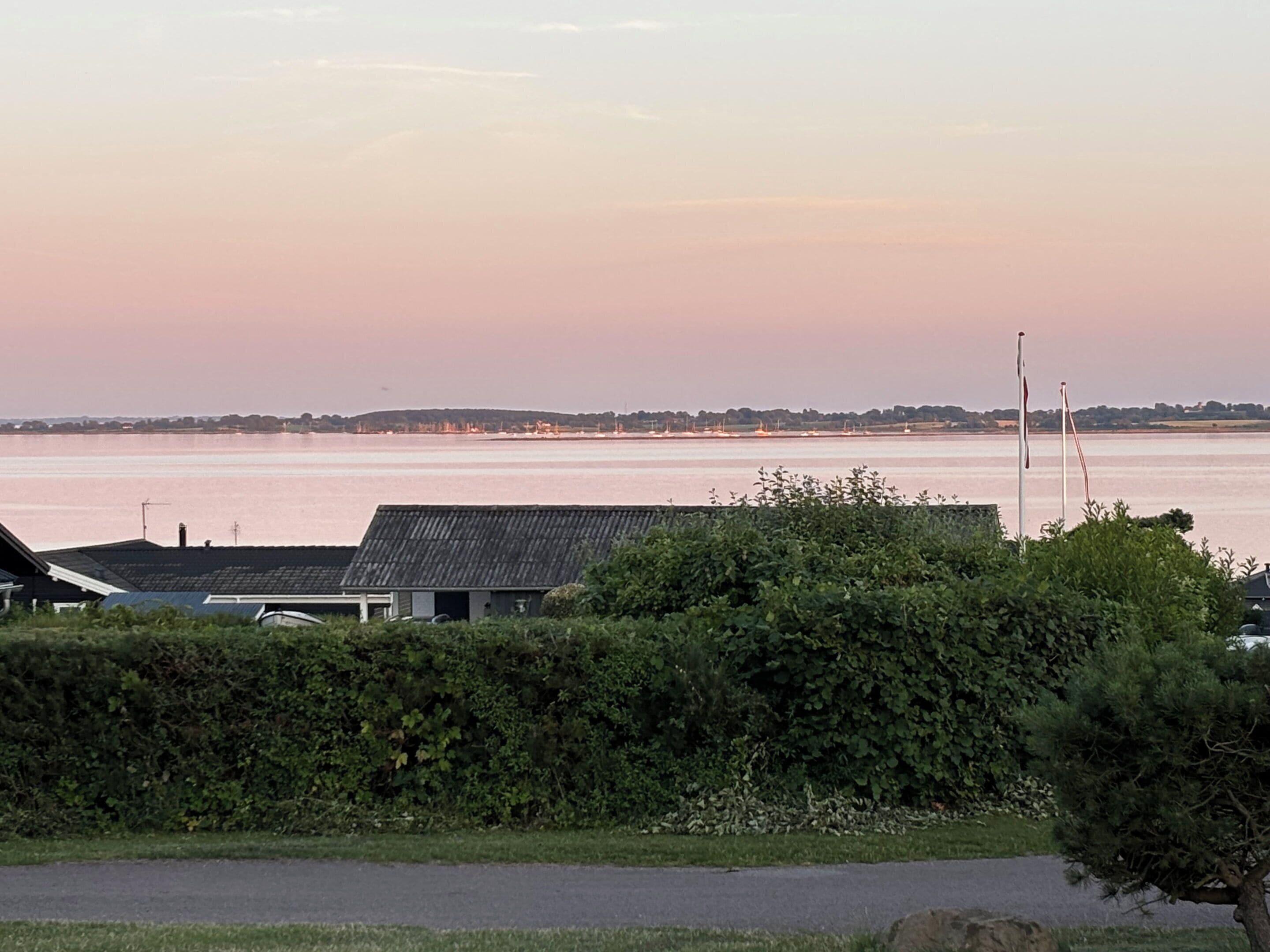 A coastal landscape with a body of water, a grassy area, and a building with a dark roof.
