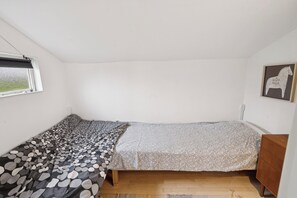 A small, single-bed room with a window, a wooden dresser, and a framed picture on the wall.