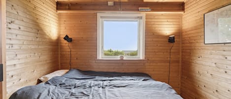 A wooden-paneled room with a bed, a window, and two wall-mounted lamps.