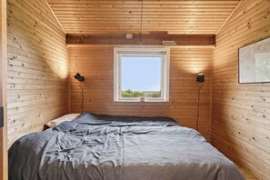 Una habitación con paneles de madera, una cama, un ventanal y dos lámparas fijadas a la pared.