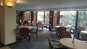 Um restaurante com mesas e cadeiras redondas, janelas amplas e vista para o exterior.