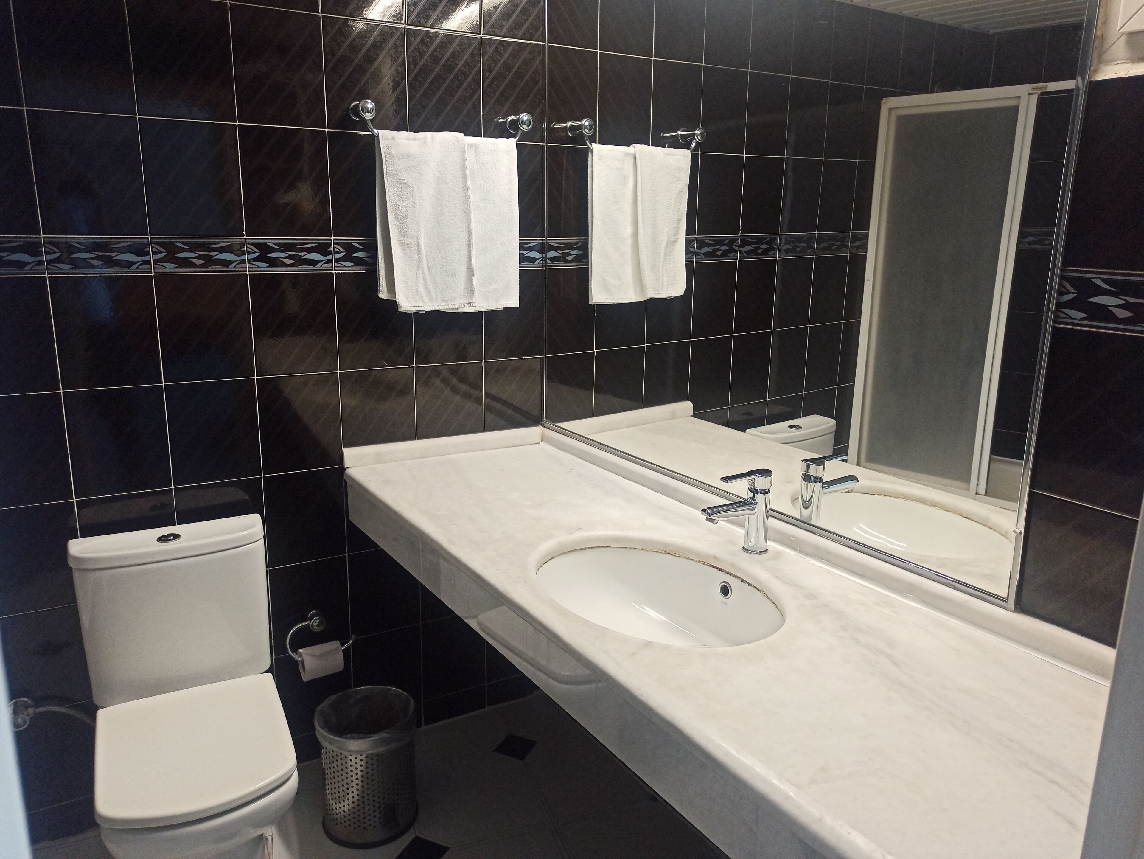 Un baño moderno con un inodoro blanco, un lavabo con espejo y dos toallas colgadas en un perchero.