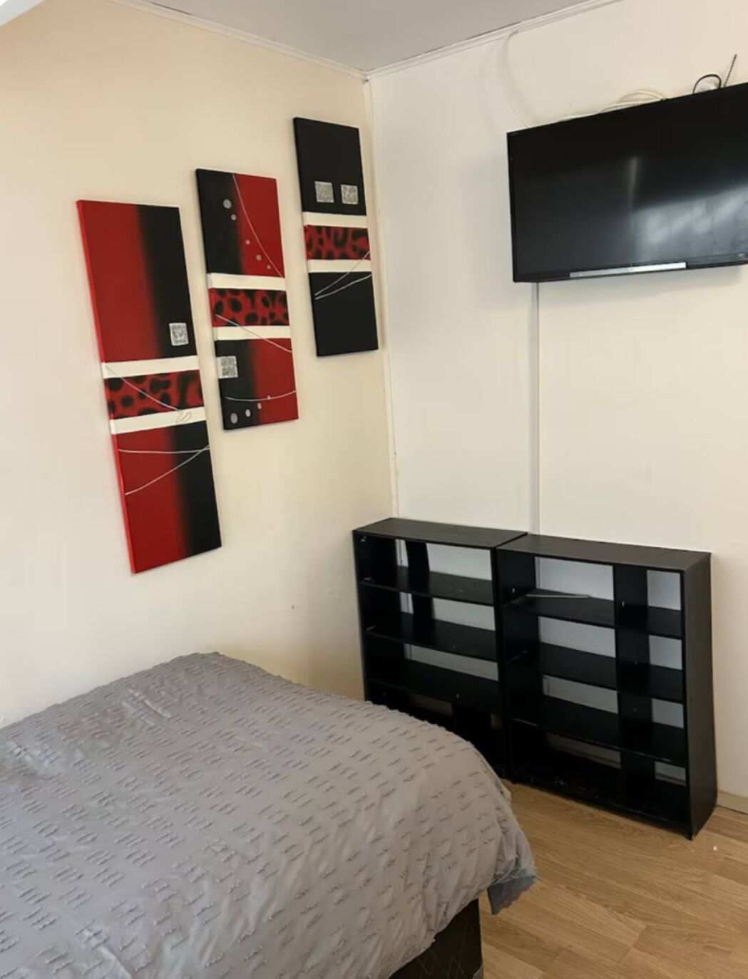A bedroom with a bed, a TV mounted on the wall, and a black shelving unit.