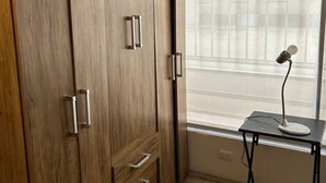 A room with a wooden wardrobe, a small table with a lamp, and a window with blinds. - Viña del Mar, nice room in a very privileged tourist sector (Viña del Mar)