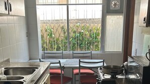 A compact kitchen with a dining table and chairs, a built-in stove, and a window with a view of greenery. - Viña del Mar, nice room in a very privileged tourist sector (Viña del Mar)