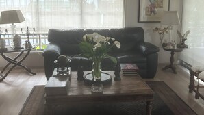 A living room with a black leather sofa, a coffee table with a vase of white flowers, and a bookshelf. - Viña del Mar, nice room in a very privileged tourist sector (Viña del Mar)