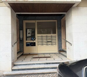 A building entrance with a double door, a small set of steps, and a car parked outside.