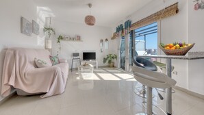 A modern living room with a sofa, a TV, a dining area with a basket of fruit, and a large window with curtains. - THE MERMAID HOUSE-PLAYA HONDA (Playa Honda)