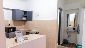 Eine kleine Küche mit Mikrowelle, Herd und einem Hängeschrank. Im angrenzenden Badezimmer sind ein Waschbecken und ein Spiegel zu sehen.