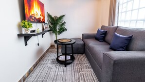 Ein modernes Wohnzimmer mit grauem Sofa, einem kleinen schwarzen Beistelltisch, einem Topfpflanzen und einem gerahmten Bild an der Wand.
