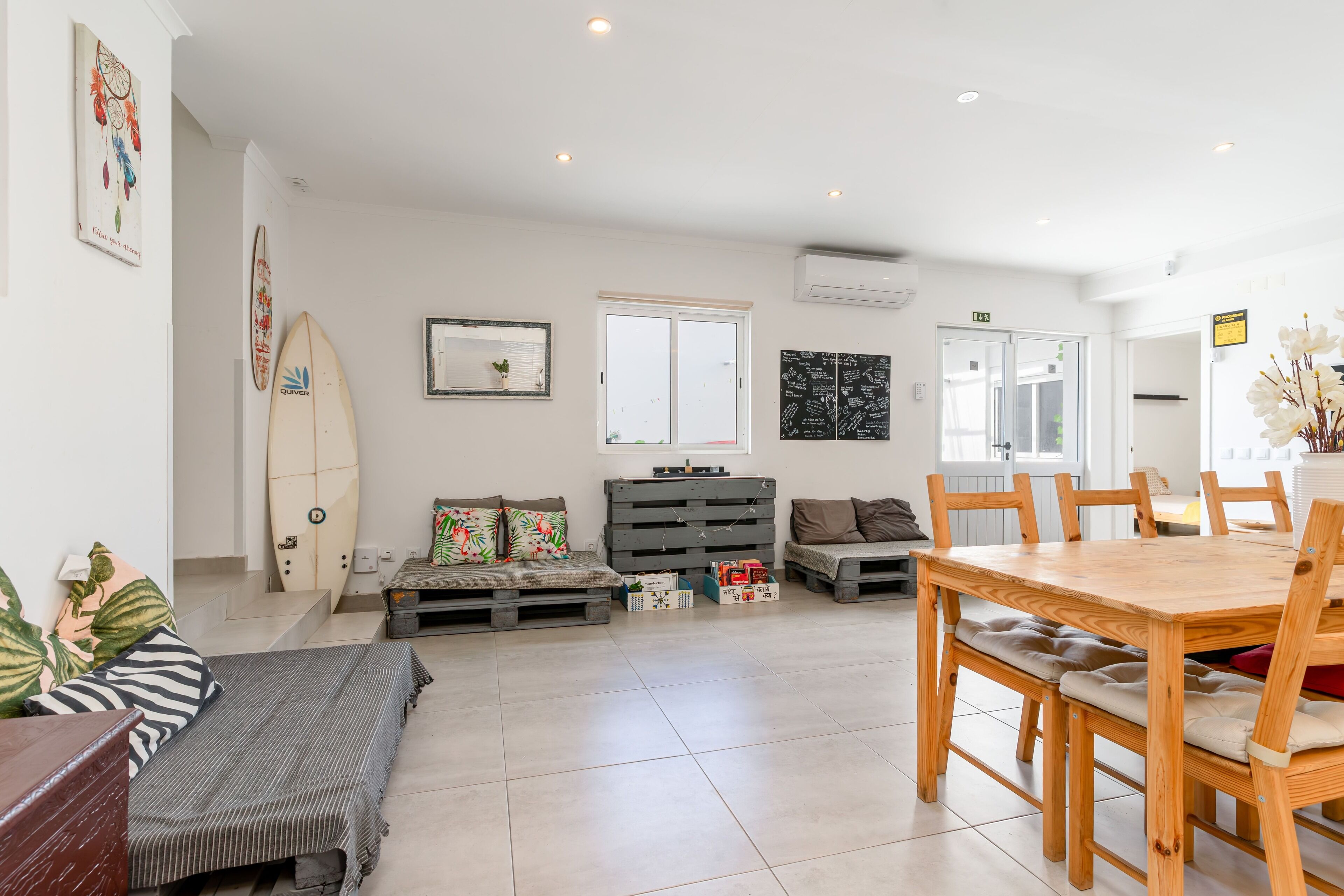 Amplia sala de estar con mesa y sillas de madera, un sofá y una tabla de surf en la pared.