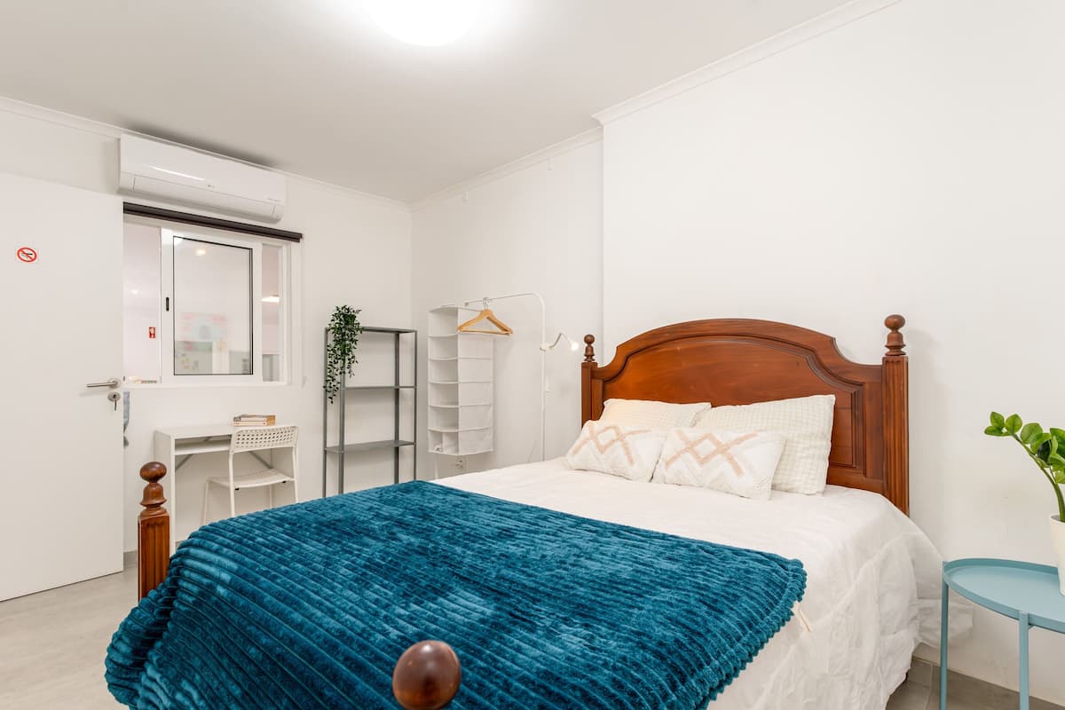 A bedroom with a bed, a bedside table, a hanging plant, and a white wardrobe.