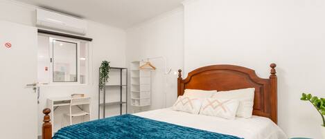 A bedroom with a bed, a bedside table, a hanging plant, and a white wardrobe.
