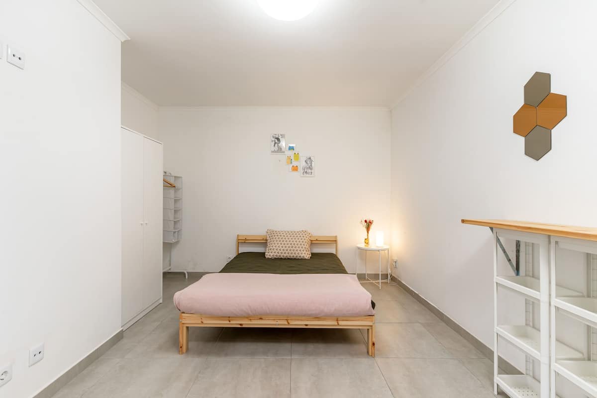A bedroom with a wooden bed, a bedside table with a lamp, a wardrobe, and a wall-mounted shelf.
