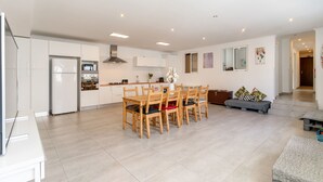Een moderne keuken met witte kasten, een eethoek met houten stoelen, en een grijze bank.