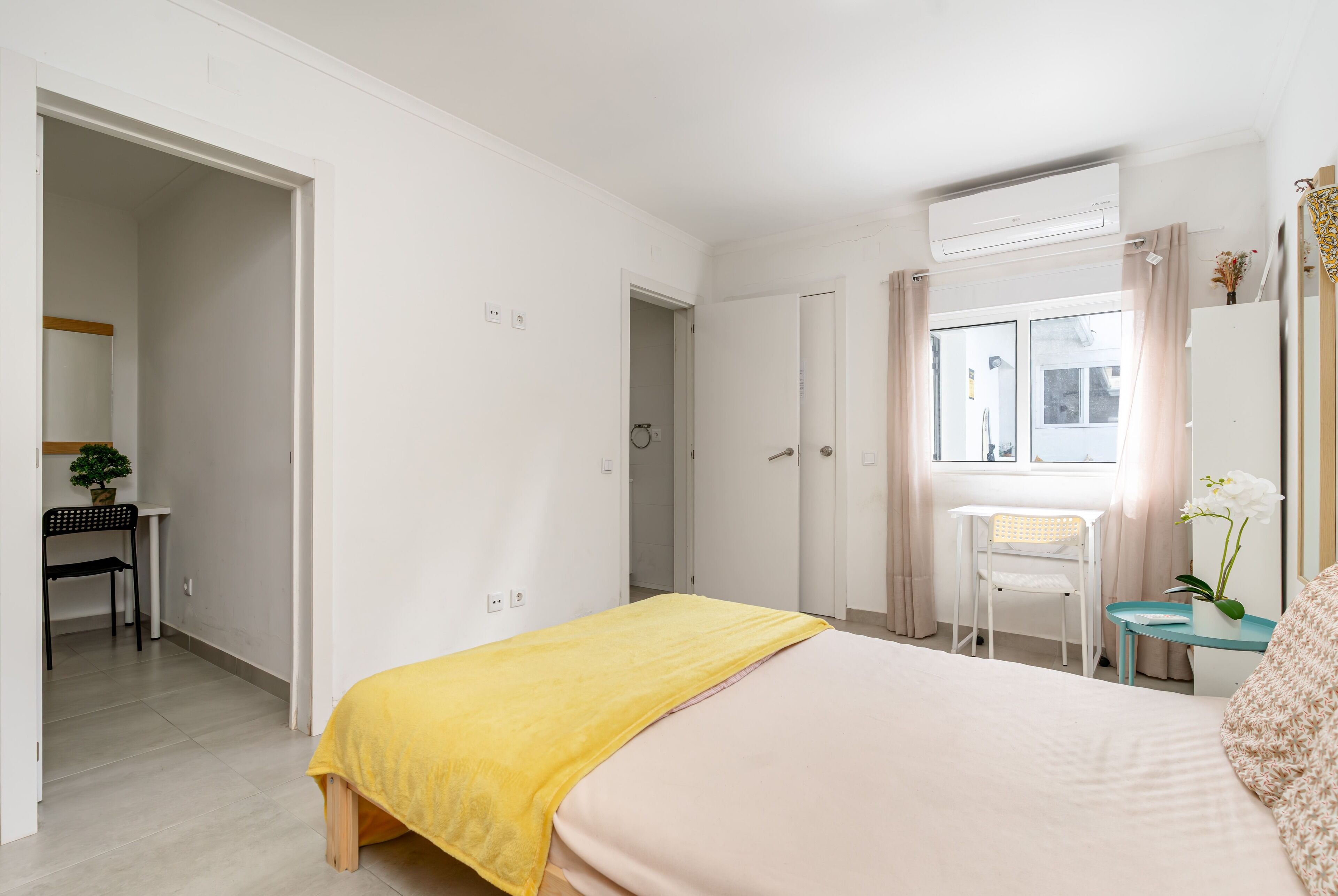 Et hotelværelse med seng, skrivebord, stol, lille bord og et vindue med gardiner.