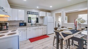 Une cuisine moderne avec des meubles blancs, un four à micro-ondes, une cuisinière et un tapis rouge.