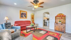 Un salon doté d’un ventilateur de plafond, d’un canapé rouge, d’un fauteuil bleu, d’une table basse et d’un meuble en bois orné d’objets décoratifs.