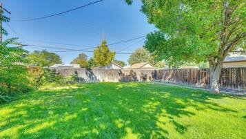 A backyard with a wooden fence, a tree, and a clear sky.