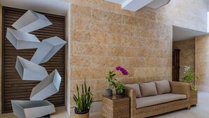 Una hall moderna con una parete in pietra, una scultura in metallo dalle forme geometriche, un divano in vimini e piante in vaso.
