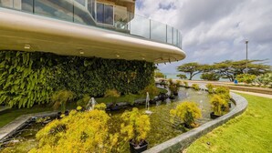 Un edificio moderno con un balcone in vetro, una parete verde rigogliosa e un elemento decorativo acquatico con piante.