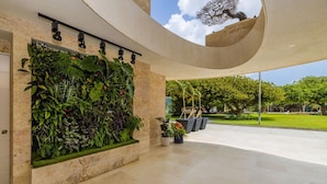 Interno di un edificio moderno con soffitto curvo, un'ampia parete verde verticale e vista su un giardino esterno curato.