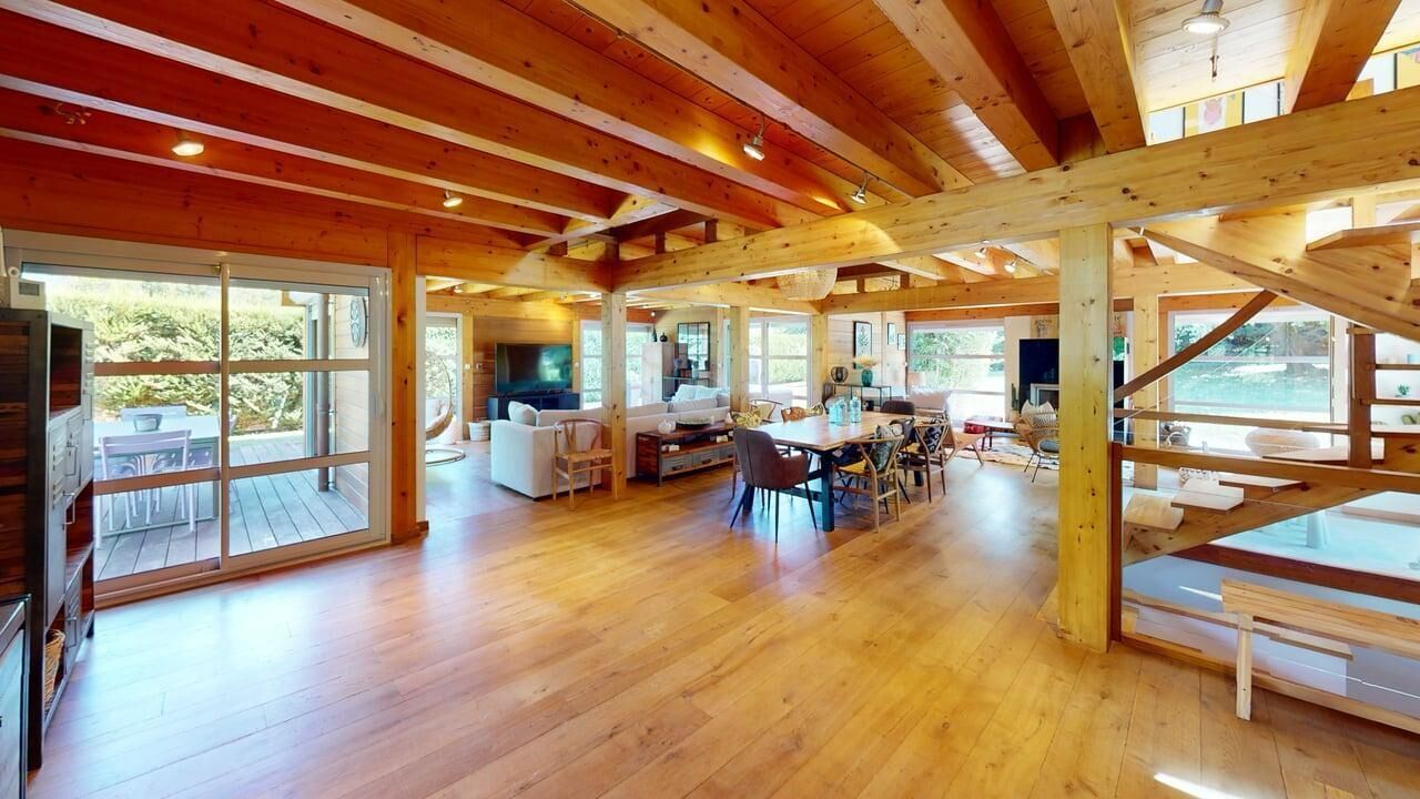 A spacious wooden interior with a large open dining area, a kitchen, and a living room with a TV.