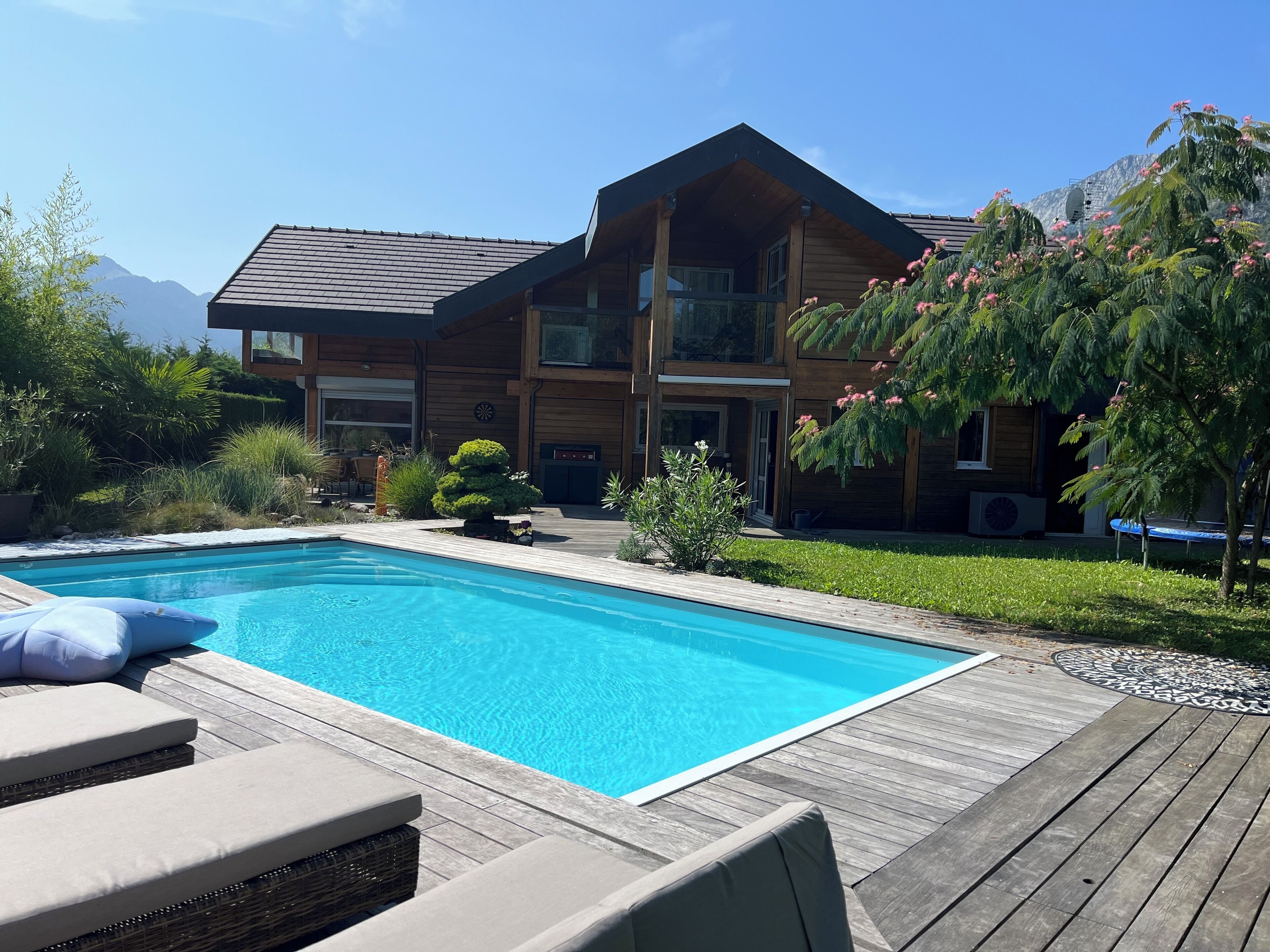 A modern two-story house with a wooden exterior, a swimming pool, and a deck with lounge chairs.