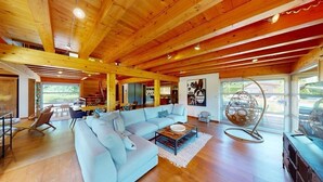 A spacious living room with a light blue sofa, wooden flooring, and a high ceiling with exposed beams. - Family House Doussard (Lake Annecy) with swimming pool (Doussard)