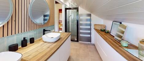 A modern bathroom with a wooden vanity, a large mirror, and a glass shower enclosure.