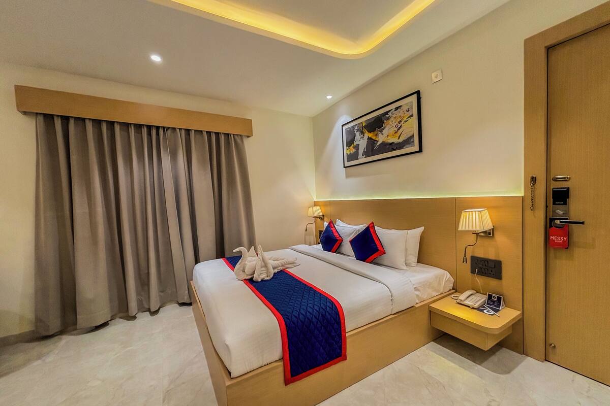 A hotel room with a large bed, a bedside table with a lamp, a phone, and a "MESSY" sign.