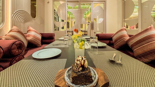 Un comedor con una mesa larga, sofás tapizados en rojo y un centro de mesa con postres.