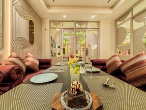 A dining area with a long table, red upholstered sofas, and a dessert centerpiece. - Zip by Spree Hotels R Group - Near Coaching Hub & Oxy Park (Kota)