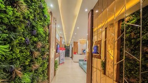 Un pasillo con una pared verde a un lado y una pared espejada al otro, que conduce a una recepción con escritorio y sillas.