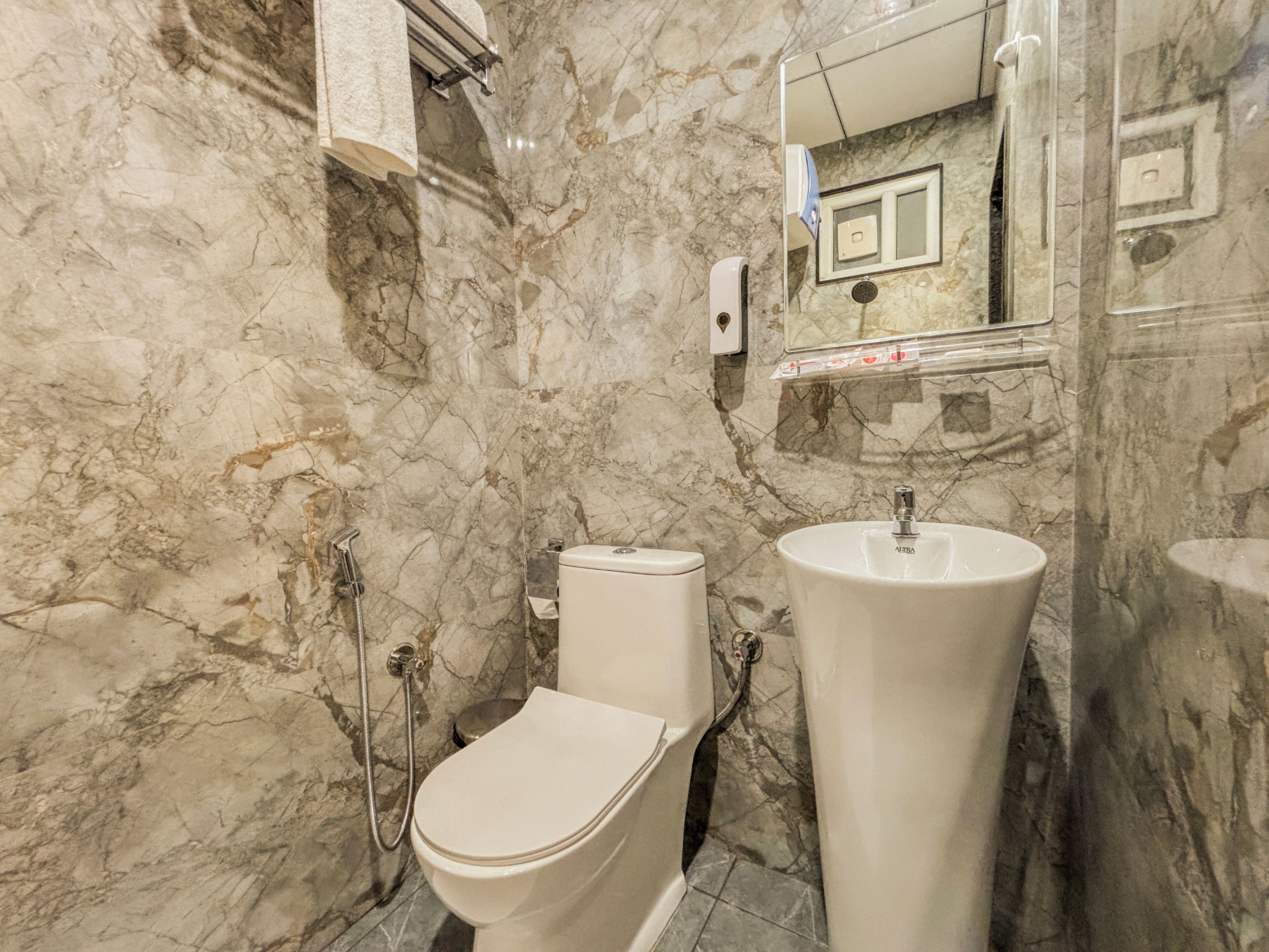 A bathroom with a marble wall, a toilet, a sink, and a mirror.