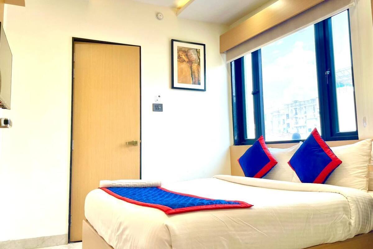 A hotel room with a bed, a door, a window, and a framed picture on the wall.
