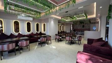 A modern interior with a seating area featuring a sofa and chairs, a dining area with tables and chairs, and a ceiling adorned with green plants and lighting.