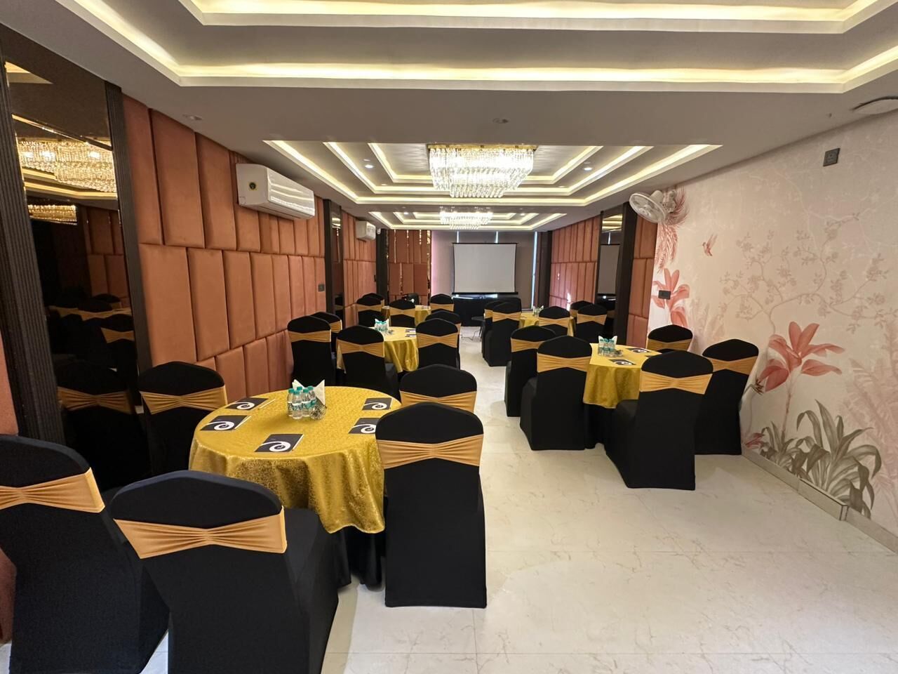 Een feestzaal met rijen tafels, zwarte stoelen met gouden linten en een kroonluchter.