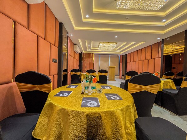 A conference room with round tables, black chairs with yellow sashes, and a chandelier.